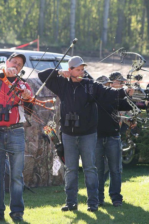 A group of men are standing in a field holding bows and arrows.