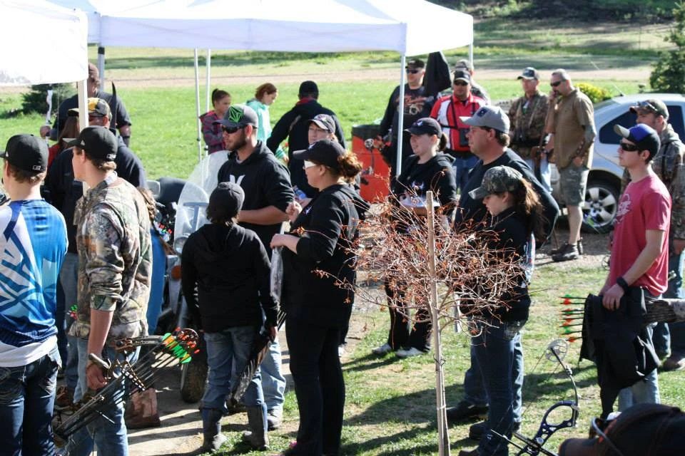 A group of people are standing under tents in a field holding bows and arrows.