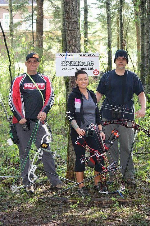 Three people are standing next to each other in the woods holding bows and arrows.