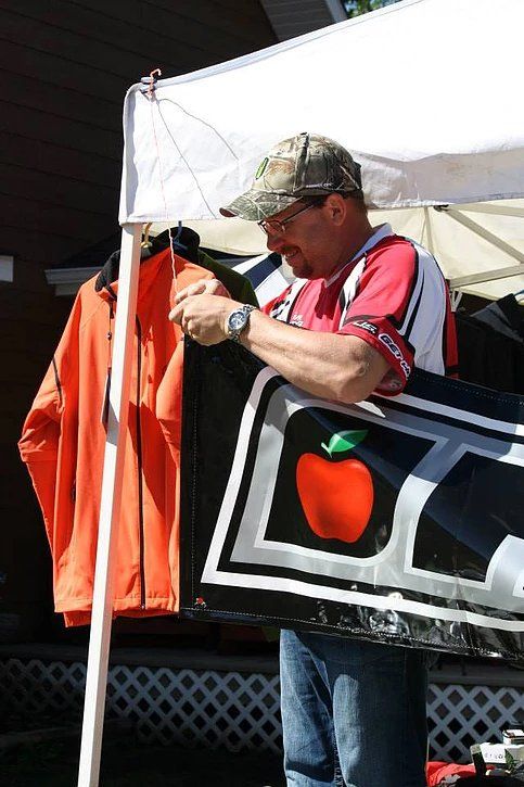A man standing under a tent holding a sign with an apple on it