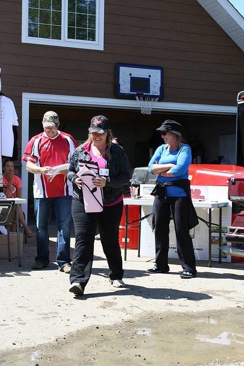 A group of people are standing in front of a garage with a basketball hoop in the background.