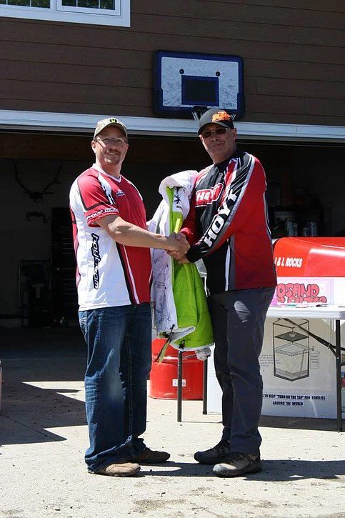 Two men are shaking hands in front of a basketball hoop.