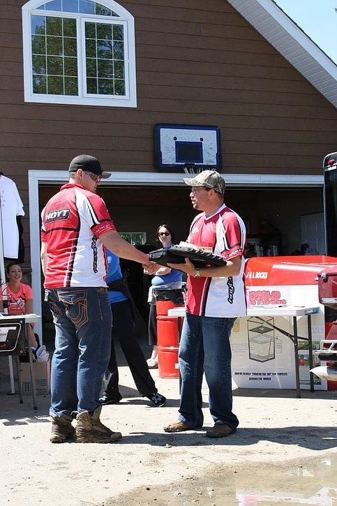 Two men are shaking hands in front of a brown house.