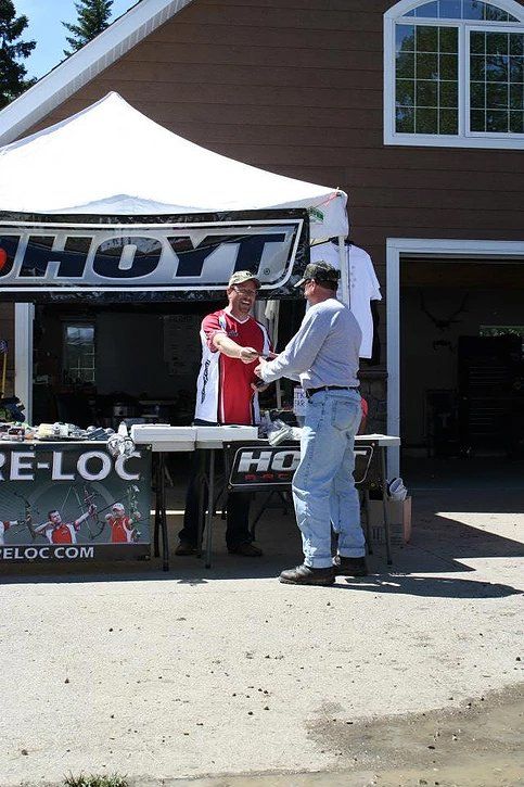 Two men are standing in front of a hoyt tent