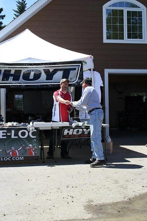 Two men shaking hands in front of a hayt tent