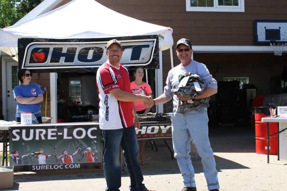 Two men shaking hands in front of a shot sign