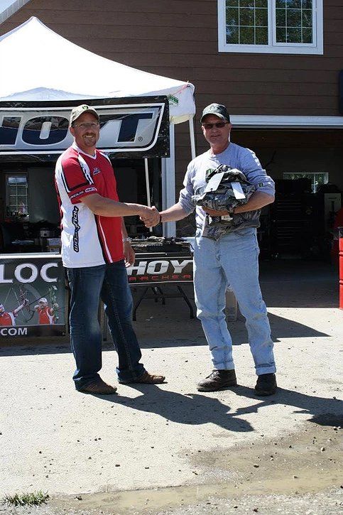 Two men shaking hands in front of a sign that says hoy