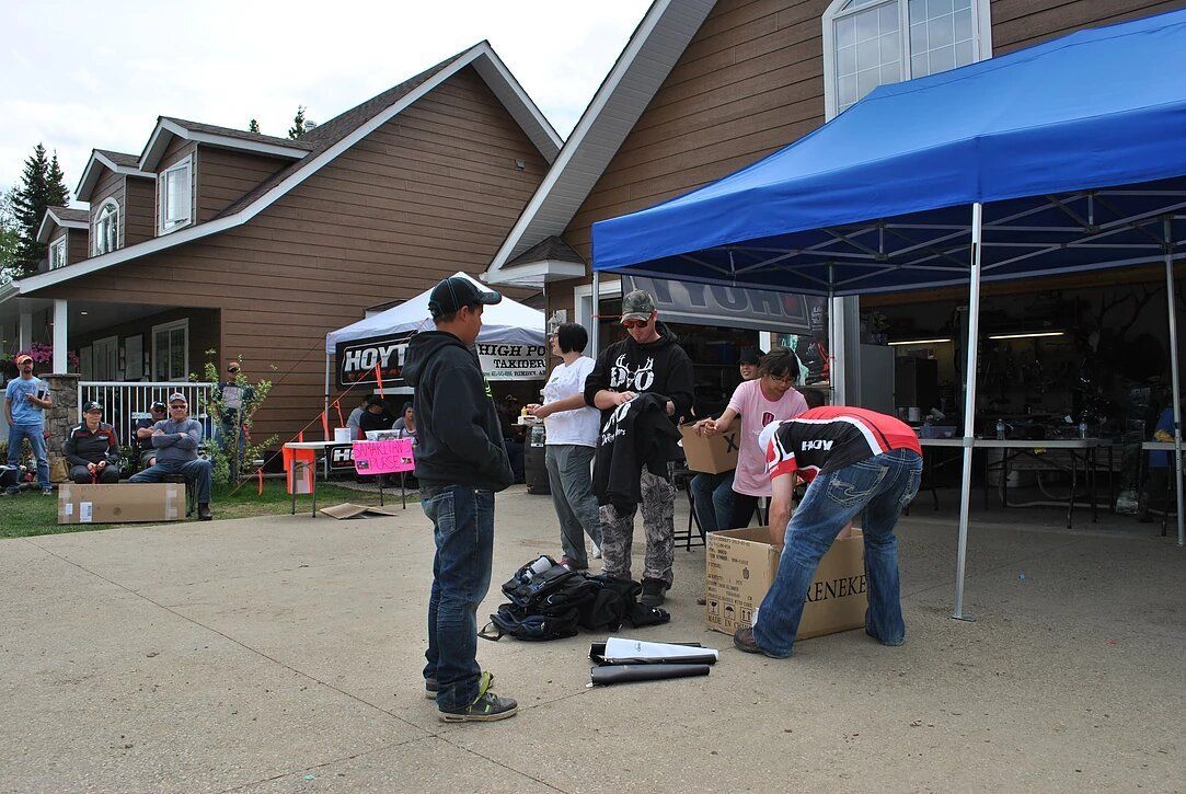 A group of people are standing under a blue tent in front of a house.