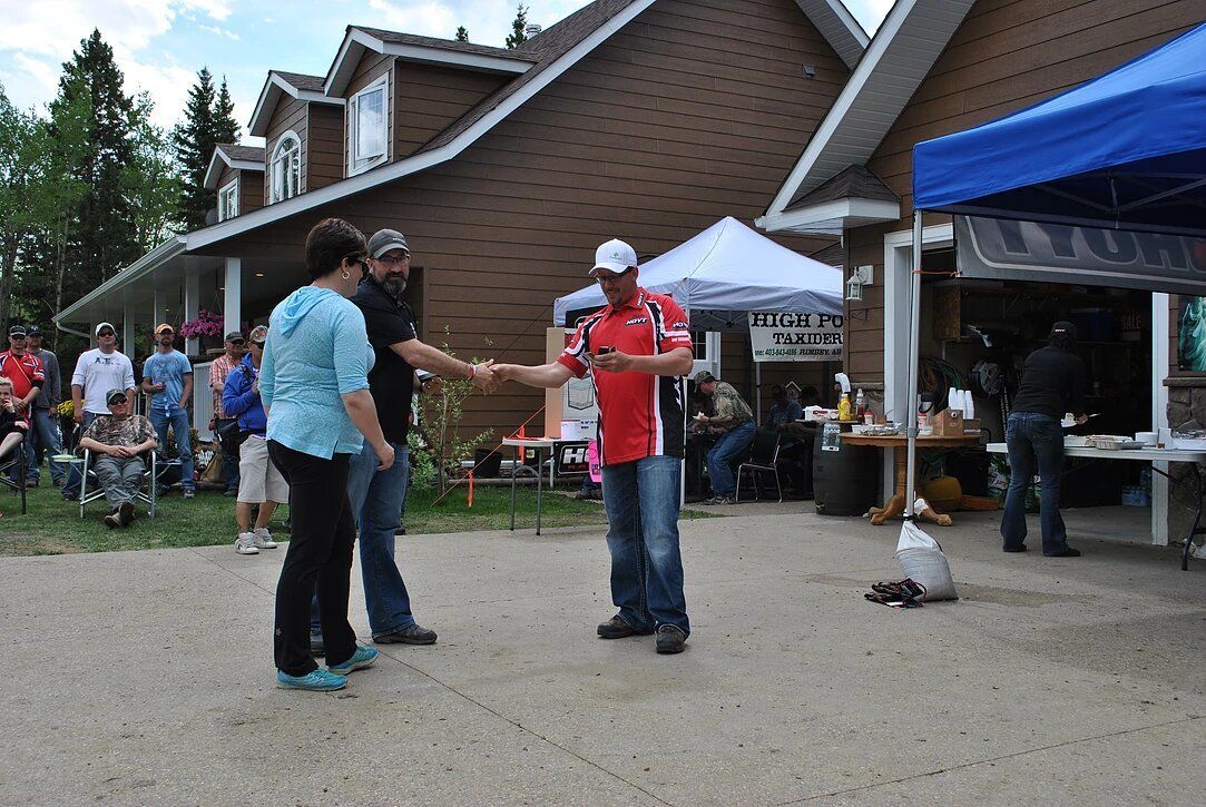 A man in a red shirt is shaking hands with a woman in front of a house.