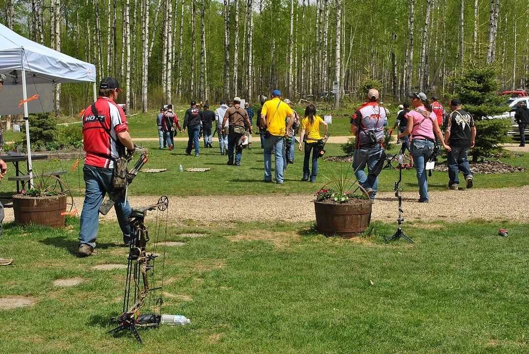 A group of people are standing in a grassy field holding bows and arrows.