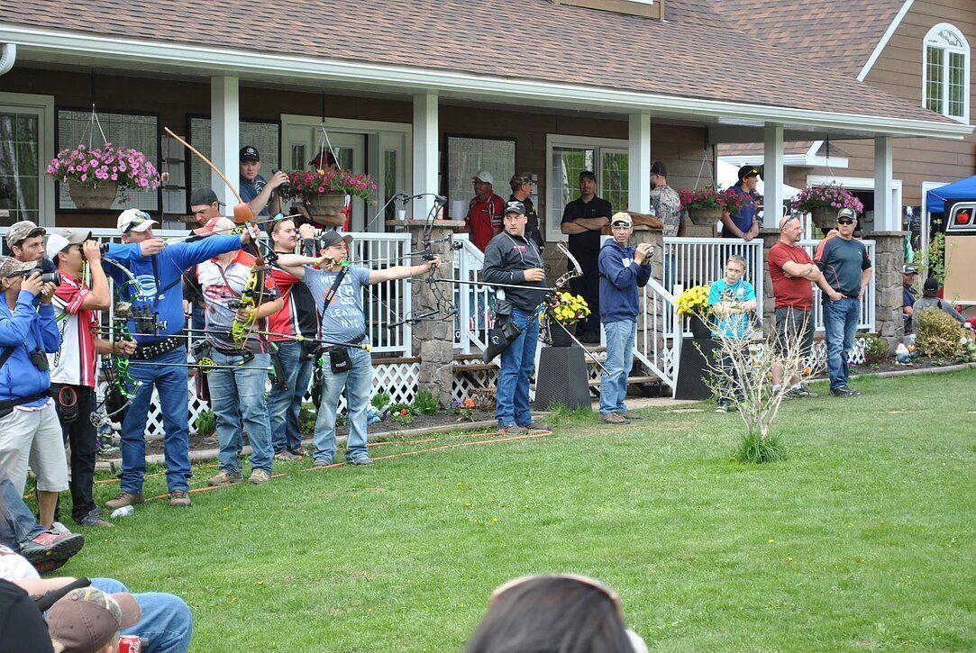 A group of people are standing in front of a house holding bows and arrows.