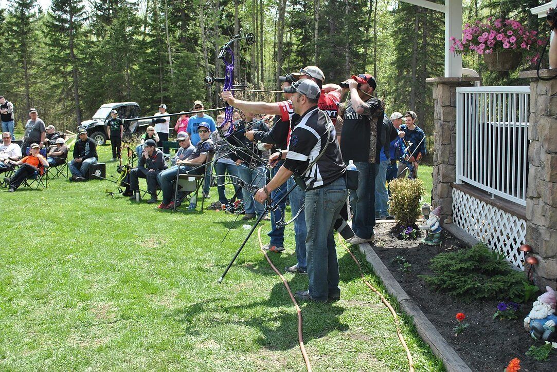 A group of people are standing in a grassy field holding bows and arrows.
