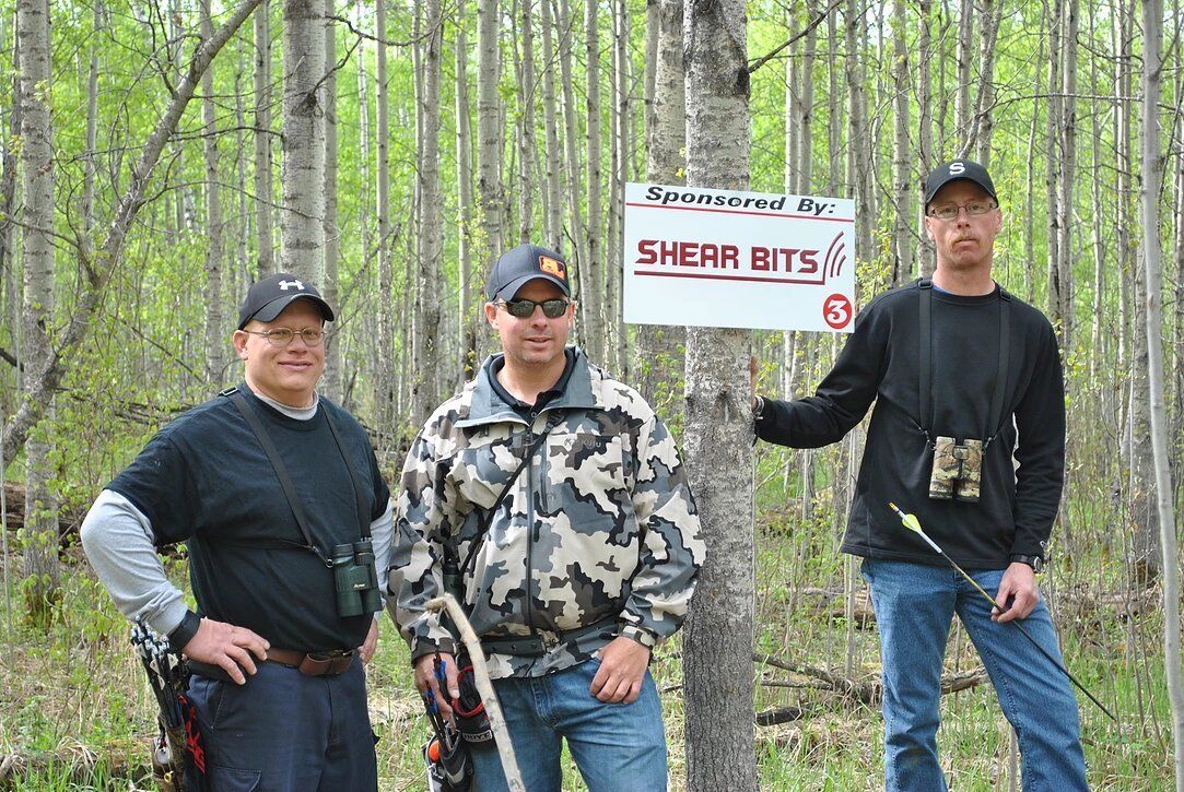 Three men are standing in the woods with a sign that says shear bits