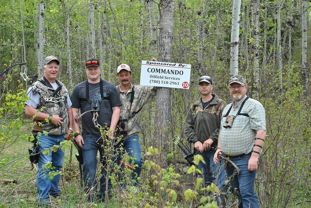 A group of men are standing in the woods holding bows and arrows.