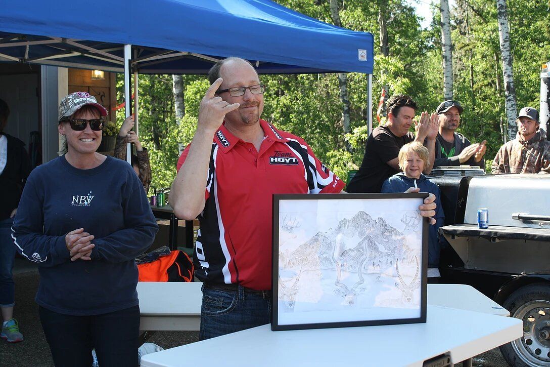 A man in a red shirt is holding a framed picture of a mountain.