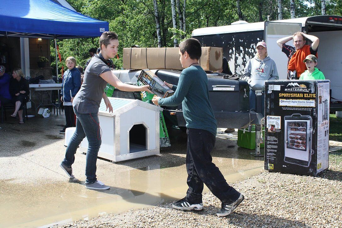A woman is helping a boy carry a dog house in a muddy area.