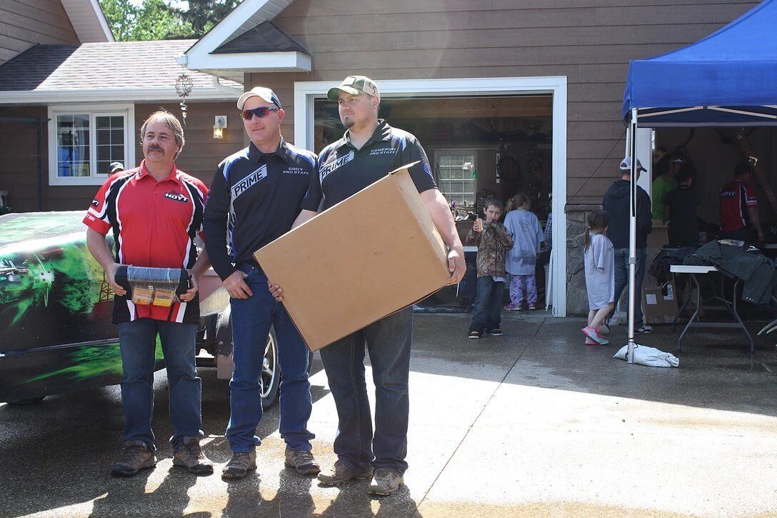 Three men are standing in front of a garage holding a cardboard box