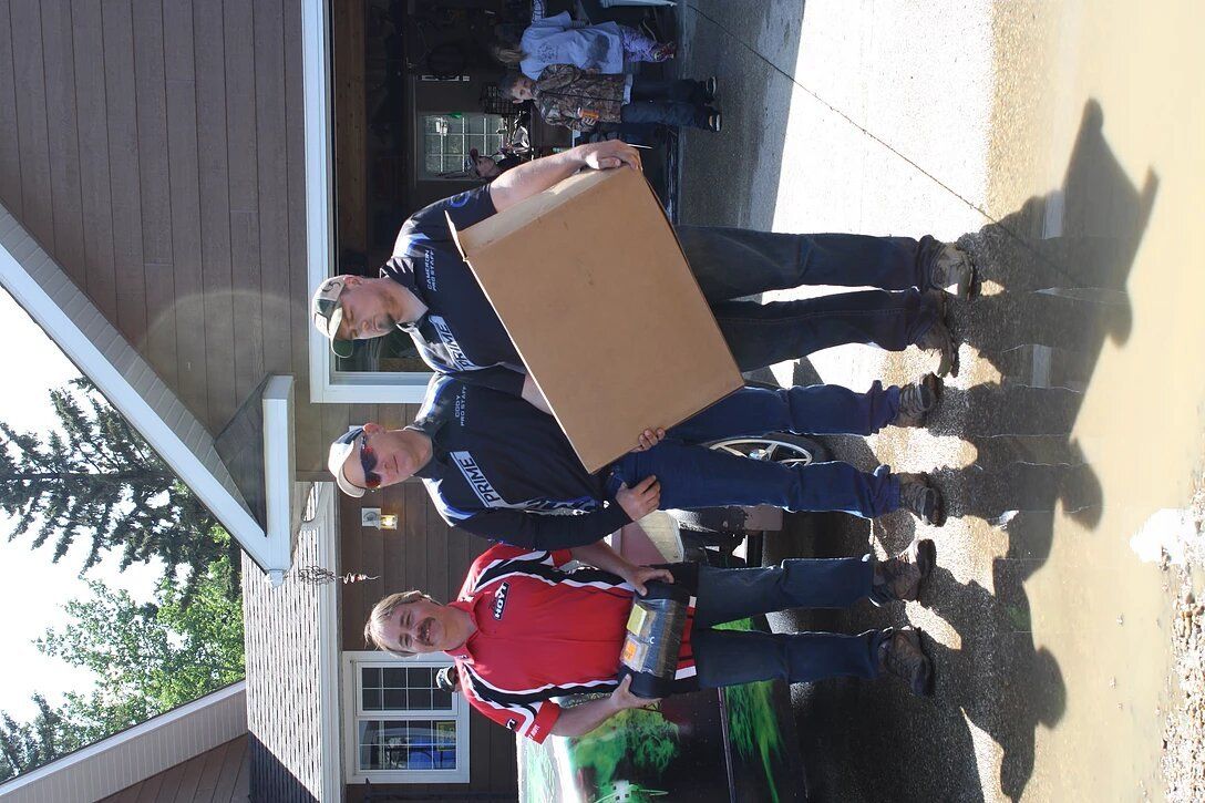 A group of people standing in front of a house holding a cardboard box