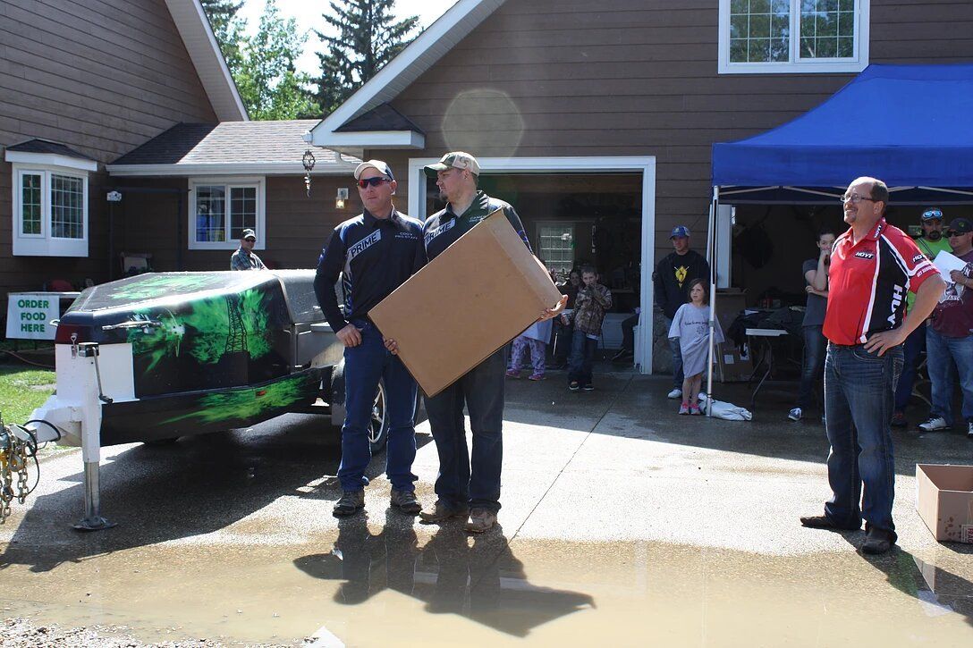 Two men are holding a cardboard box in front of a house