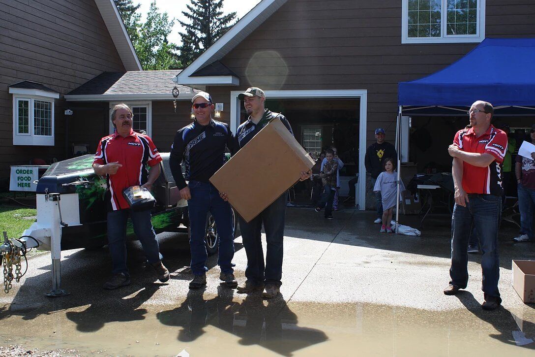 A group of men are standing in front of a house holding a cardboard box