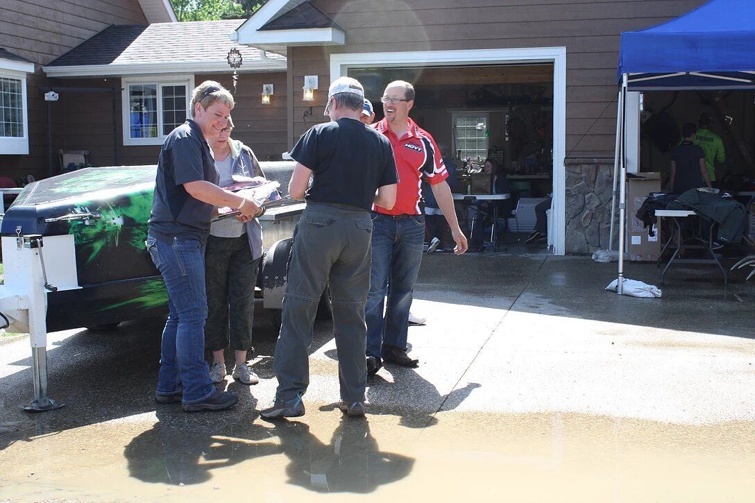 A group of people are standing in front of a car in a driveway.
