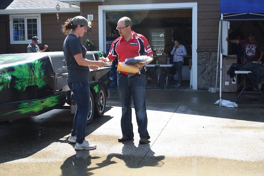 A man and a woman are standing in front of a car in a driveway.