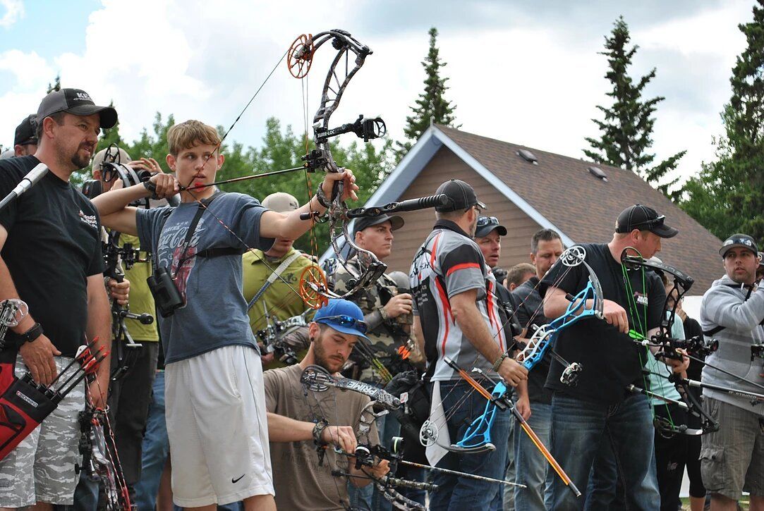 A group of people are holding bows and arrows in front of a house.