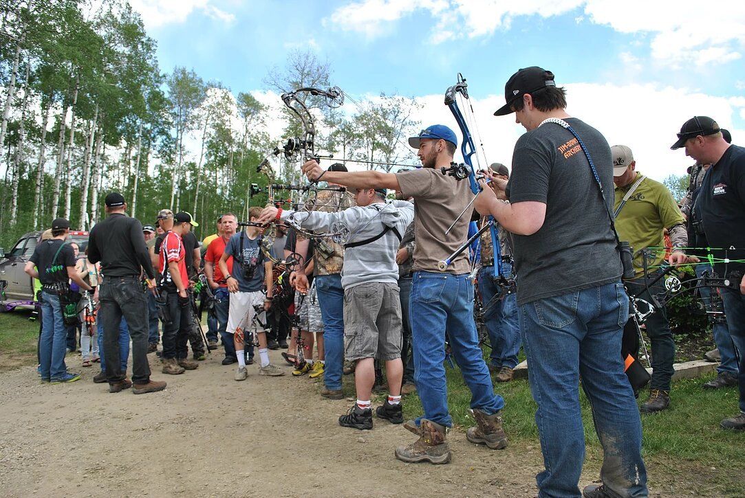 A group of men are standing in a field holding bows and arrows.