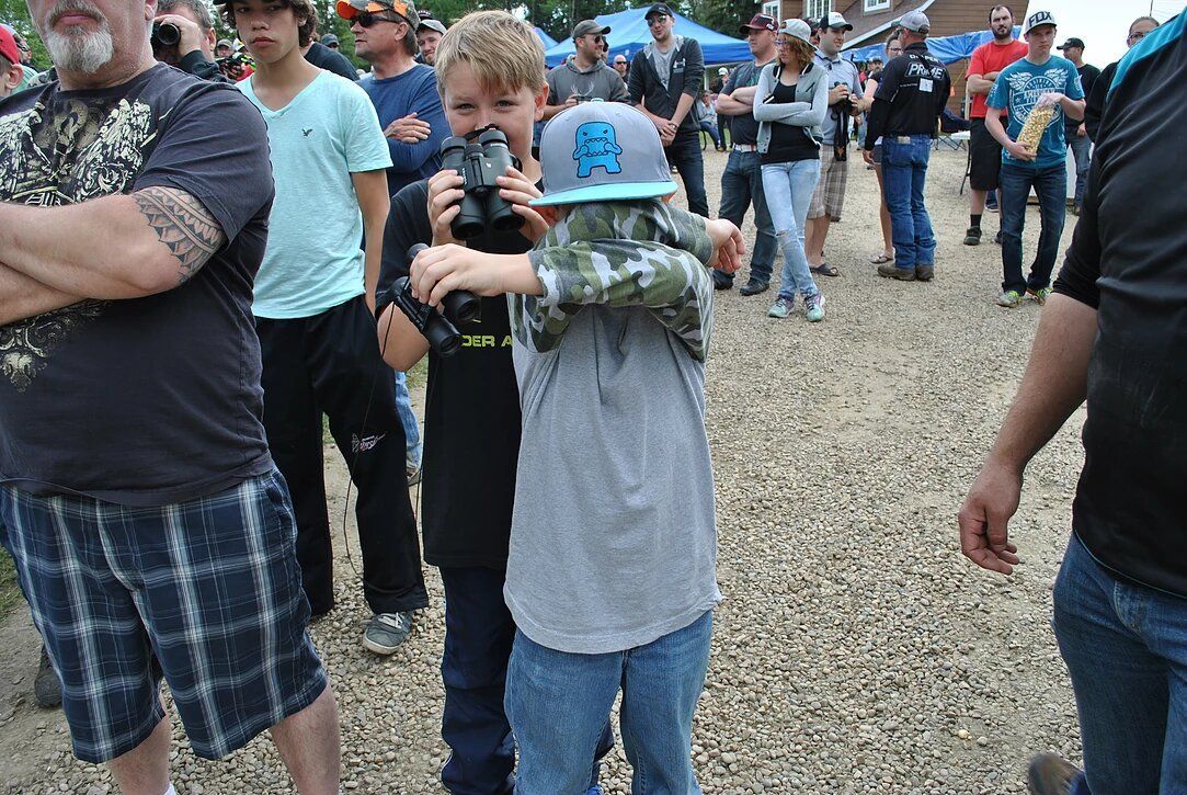 A group of people are standing in a dirt field and one boy is wearing a hat that says nc