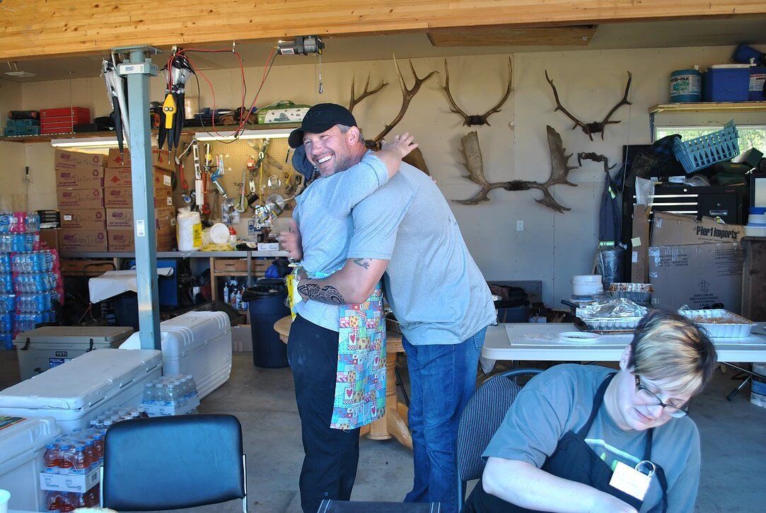 A man is hugging another man in a room with antlers on the wall.