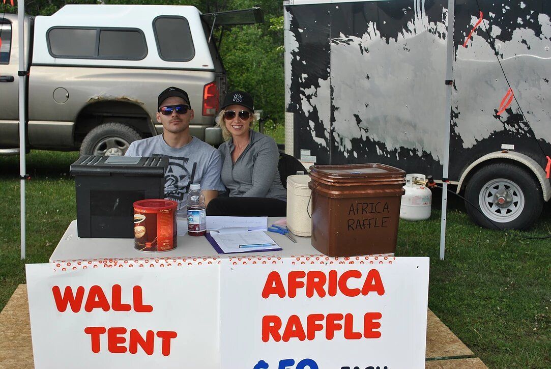 A man and woman sitting at a table with a sign that says wall tent africa raffle