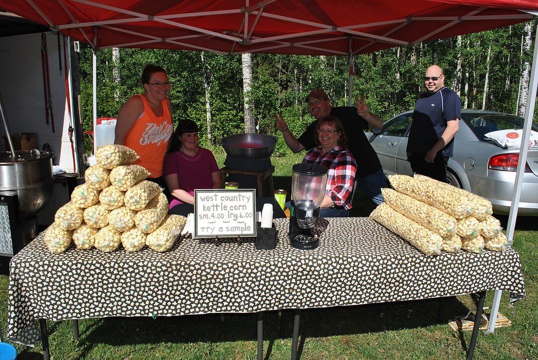 A group of people are standing around a table selling pop corn.