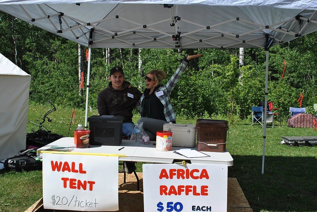 A man and a woman are standing under a tent selling wall tents and africa raffle