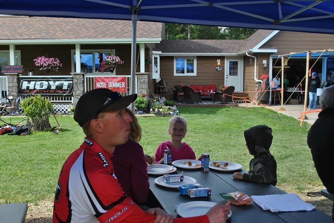 A group of people are sitting at a picnic table in front of a house.