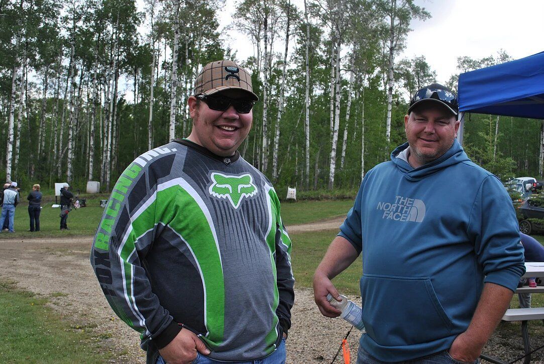 Two men standing next to each other in a field with trees in the background