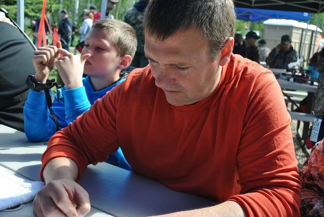 A man in an orange shirt is sitting at a table with a boy in a blue shirt behind him.