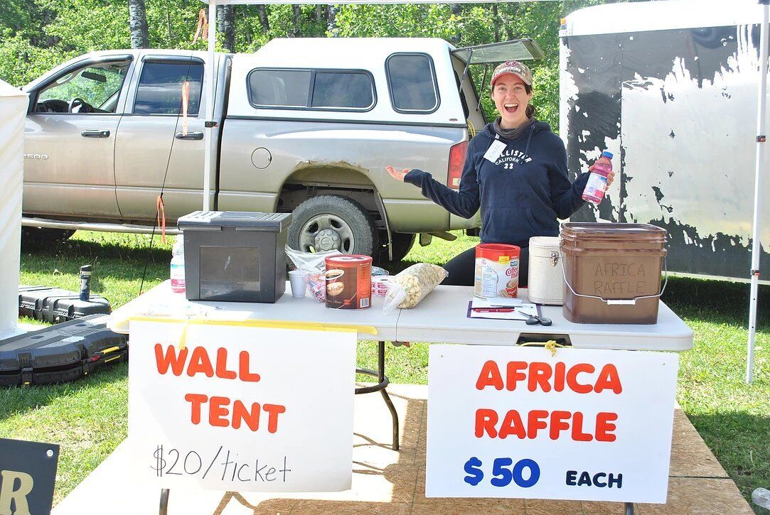 A woman is standing behind a table with a sign that says africa raffle $ 50 each.
