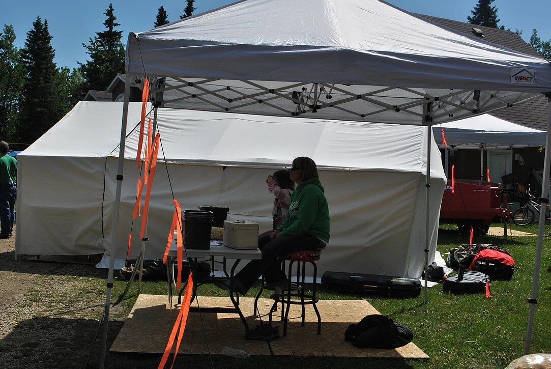 A man sits on a stool under a white tent