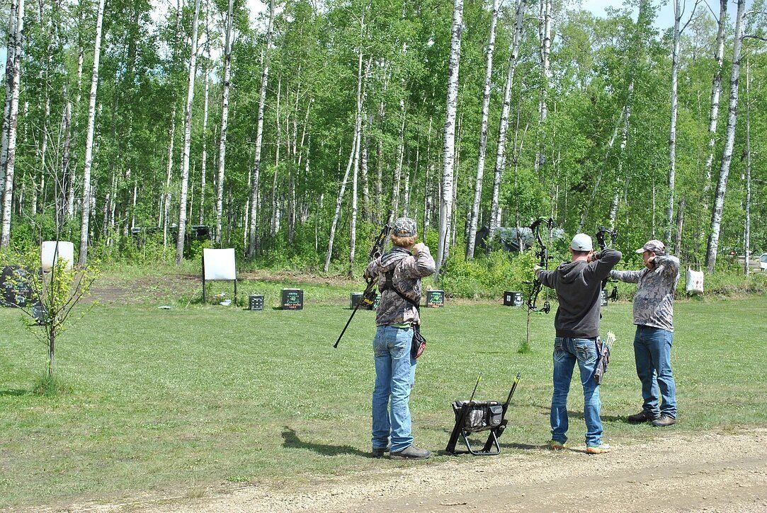 Three men are practicing archery in a field with trees in the background.