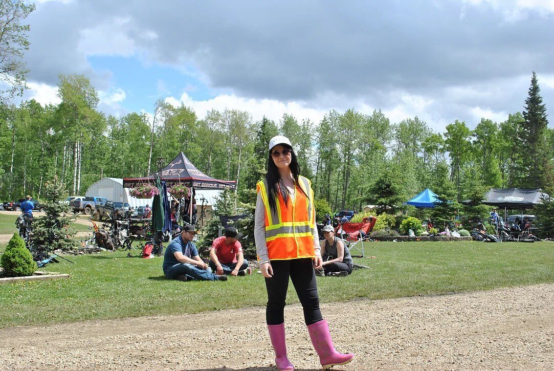 A woman wearing a safety vest and pink boots is standing in a park.