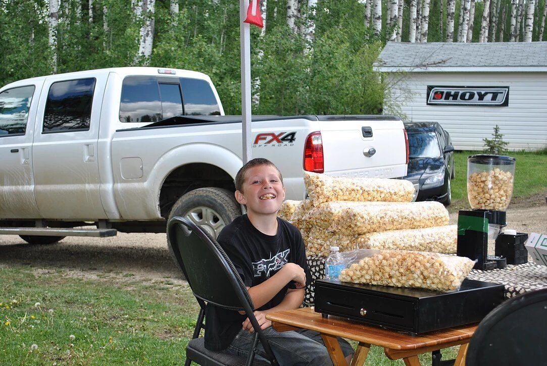 A boy is sitting at a table with a truck in the background.