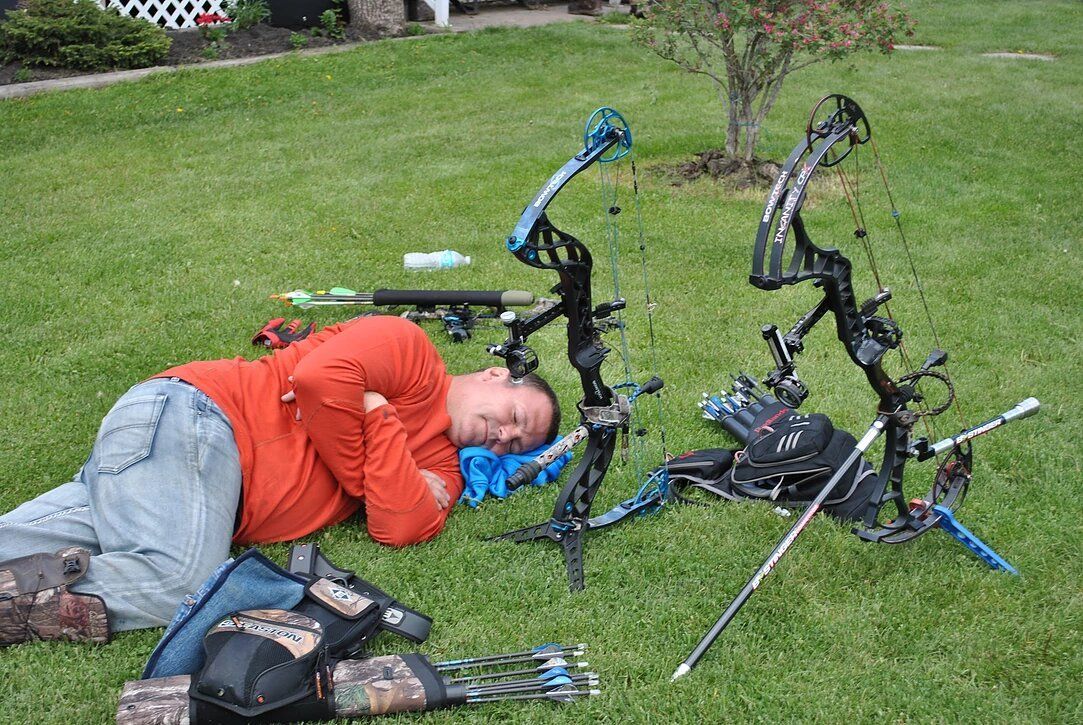 A man is laying on the grass next to bows and arrows.