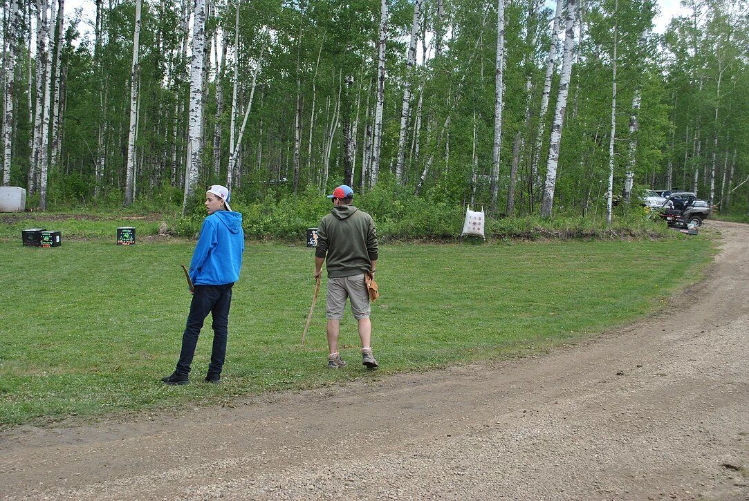 Two men are standing in a grassy field next to a dirt road.
