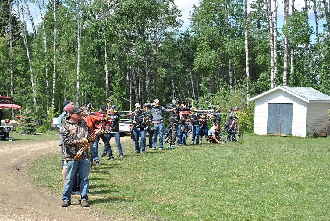A group of people are standing in a grassy field with trees in the background.