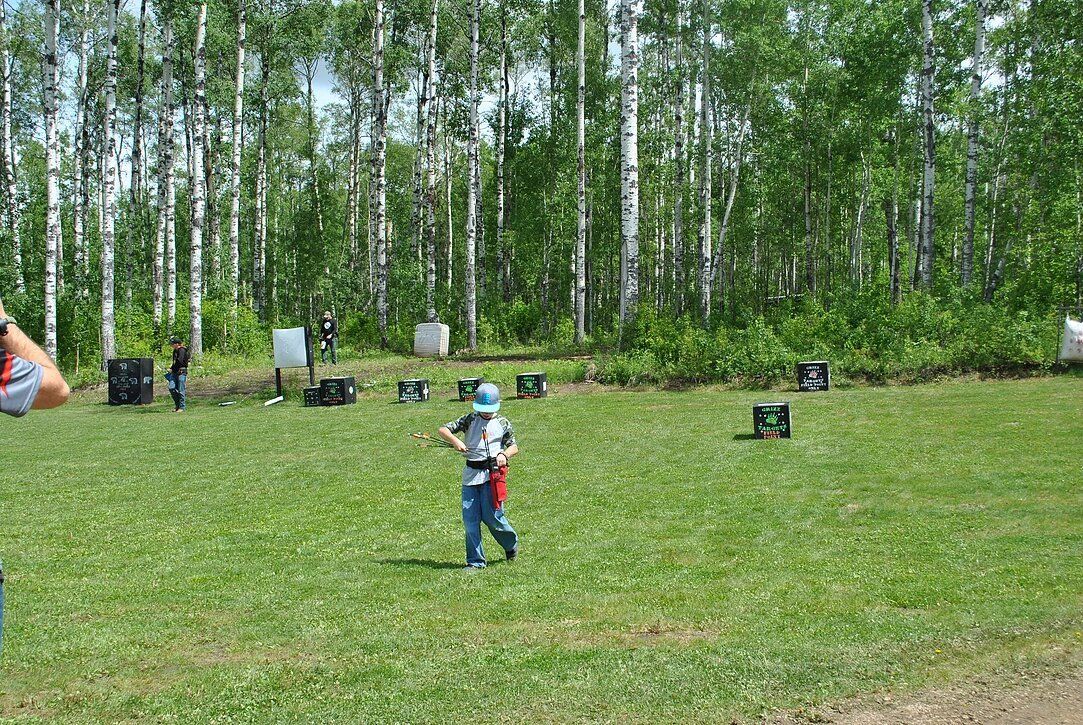 A little boy is playing paintball in a field with trees in the background.