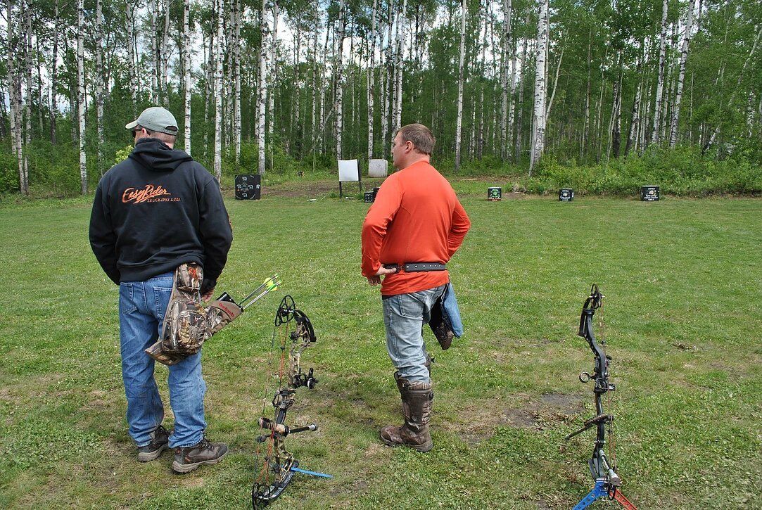 Two men are standing in a field with bows and arrows.