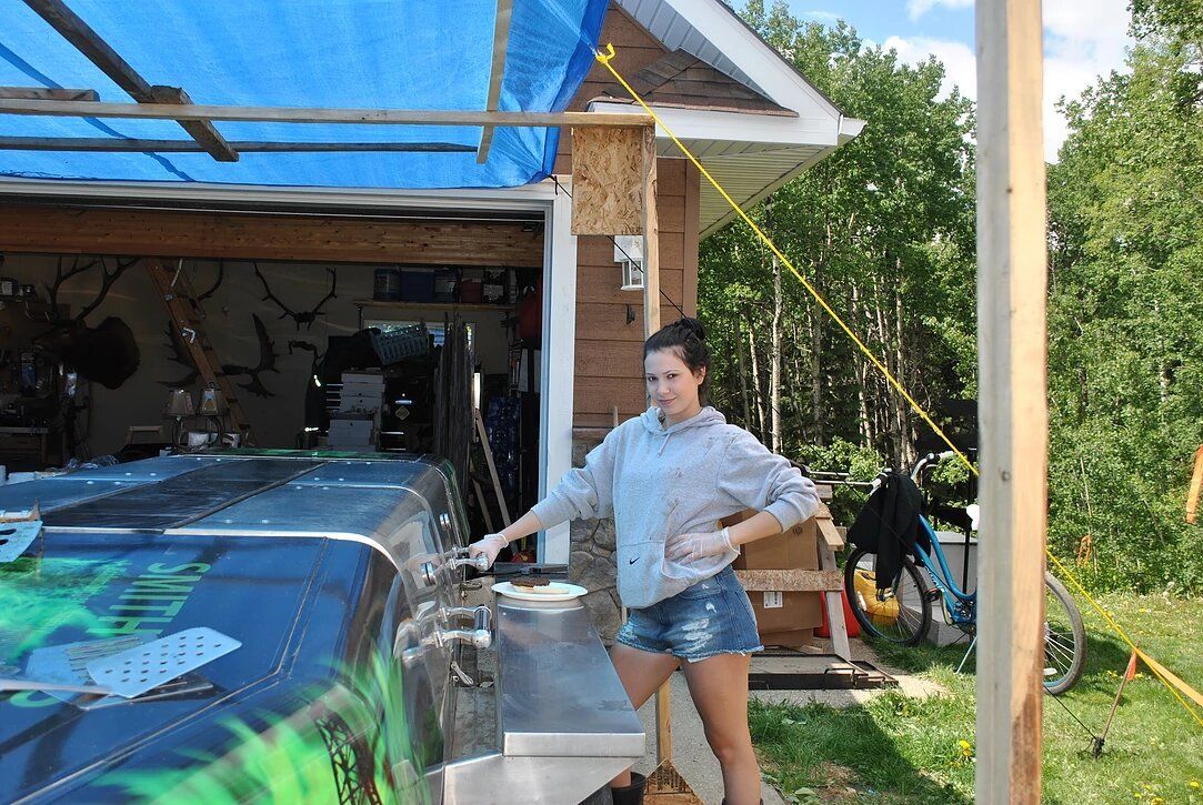A woman is standing in front of a garage with a blue tarp on the roof.