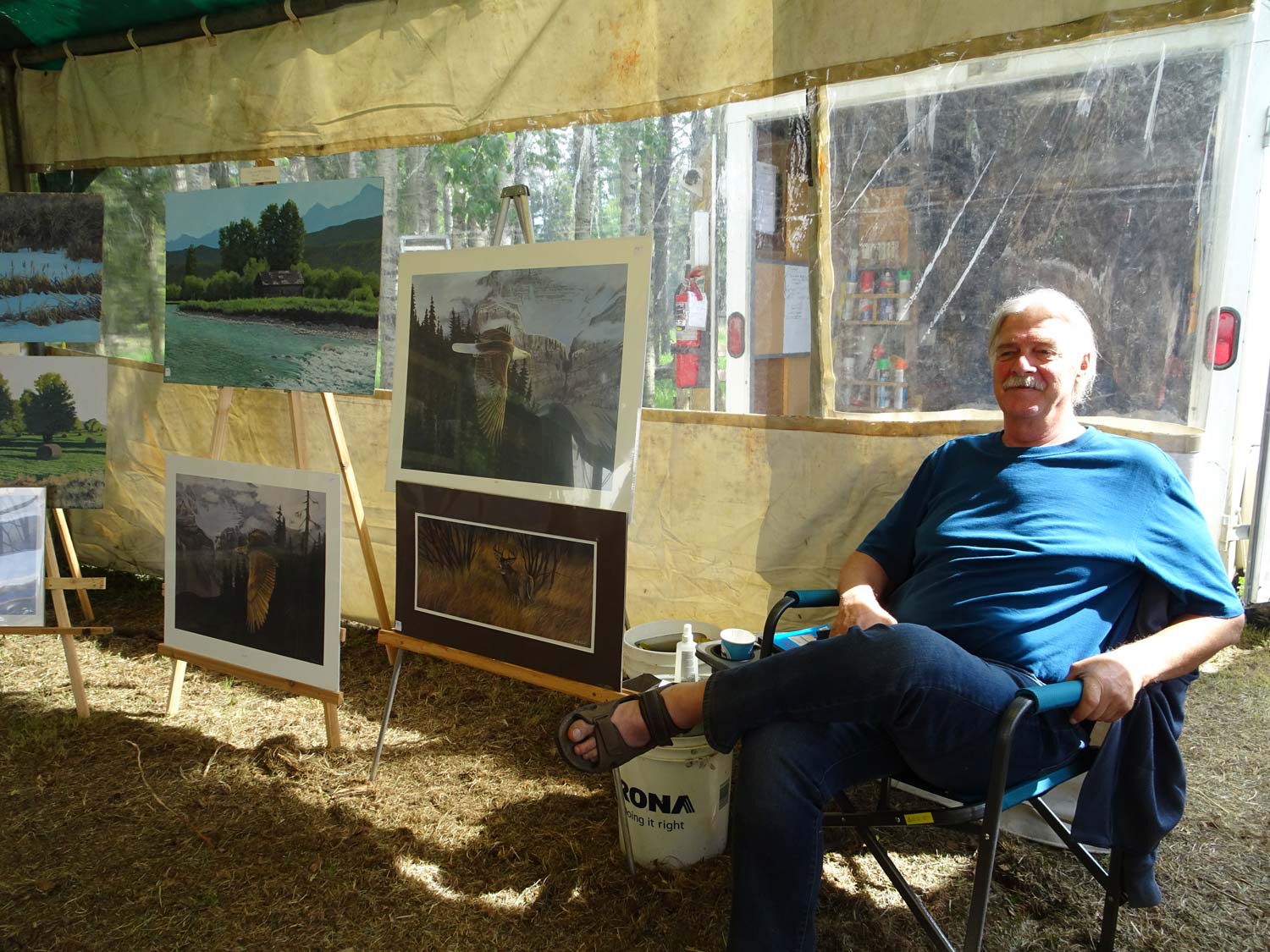 A man in a blue shirt is sitting in a chair in front of paintings.