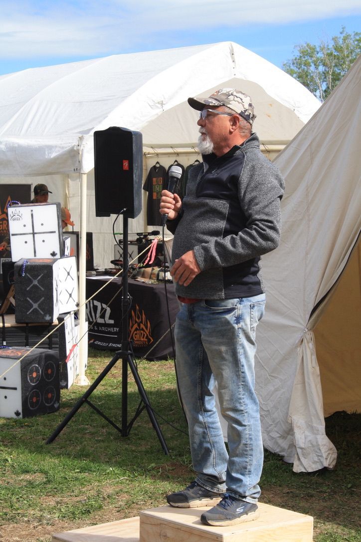A man is standing on a podium holding a microphone in front of a tent.
