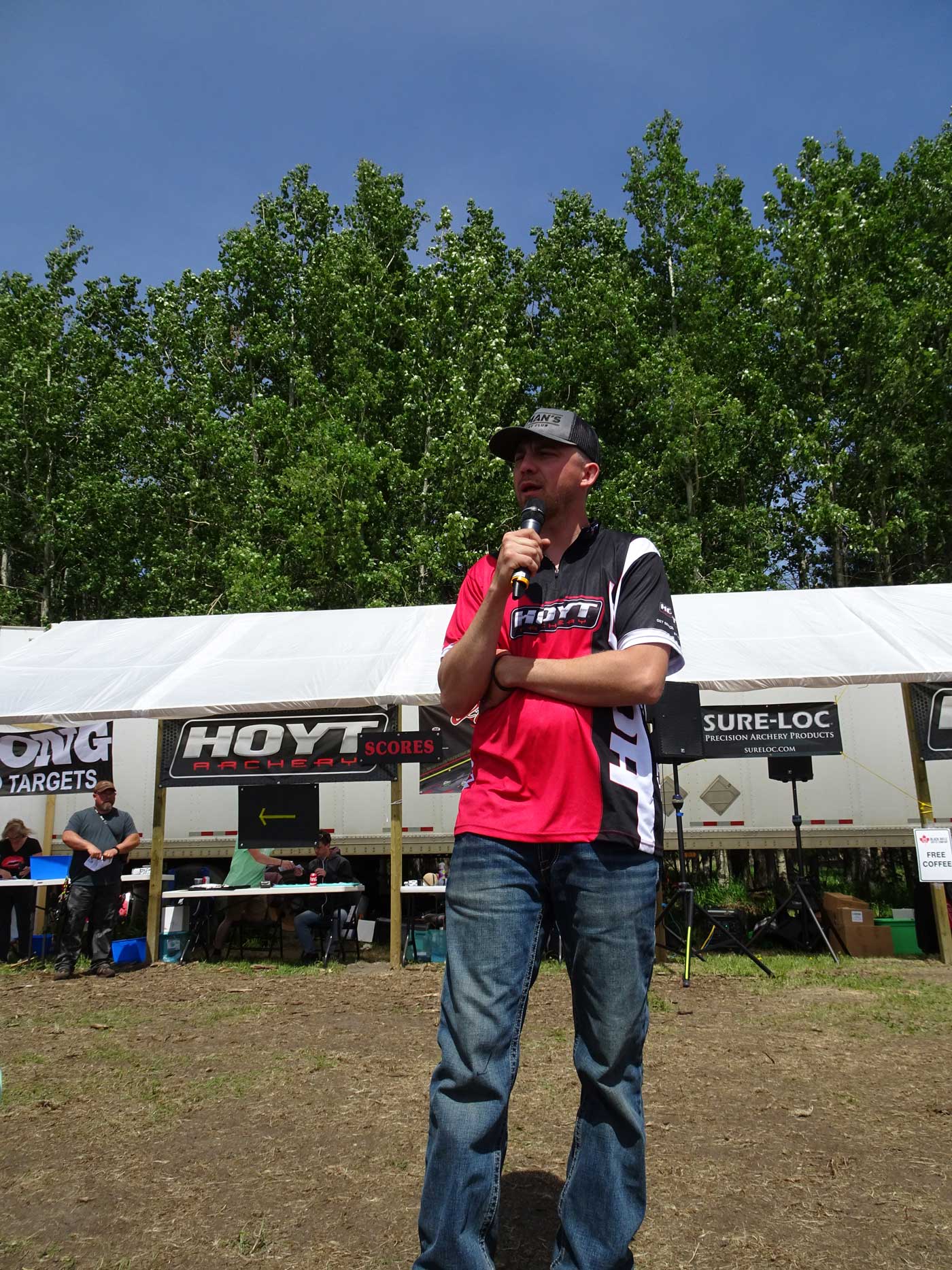 A man speaking into a microphone in front of a hayt tent